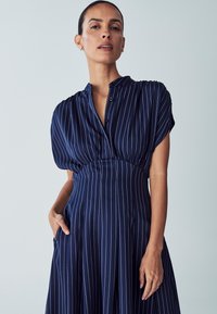 Navy dress with white vertical stripes, short puff sleeves, buttoned collar, and side pockets; smooth fabric with a fitted bodice and flared skirt.