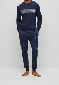 Marinblå sweatpants och långärmad topp med ett grått horisontellt rand, båda med guld "BOSS"-logotypdetaljer. Mjuk, strukturerad tyg.
