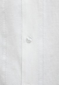 White button fastened on a textured fabric shirt with vertical stitched stripes in close-up view.
