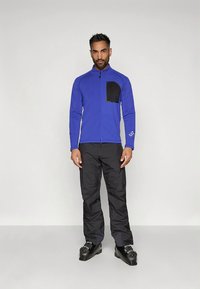 Μπλε μπουφάν με φερμουάρ και μαύρη τσέπη στο στήθος, σε συνδυασμό με μαύρο παντελόνι και μαύρα παπούτσια. Λείο ύφασμα με εφαρμοστή σχεδίαση.