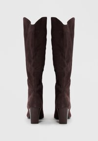 Bottes en suède marron jusqu'au genou avec un bord supérieur pointu, un large talon et des zips sur les côtés pour un enfilage facile. Texture lisse avec une finition mate.