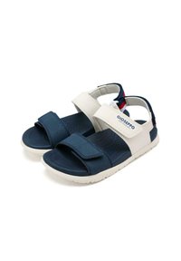 Sandali per bambini blu marina e bianchi con cinturini in Velcro, suola strutturata e sottopiede imbottito. Presentano il logo sul lato e dettagli sul cinturino posteriore.