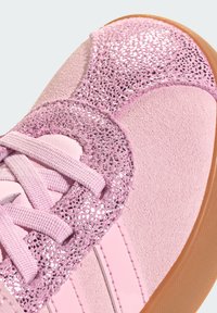 Pink sneaker with suede material, sparkly glitter accent, and textured laces. Features rubber sole and shiny pink stripes.