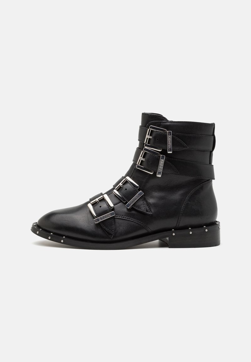 Botas de tobillo de cuero negro con tres correas de hebilla, puntera afilada y acentos de tachuelas plateadas a lo largo de la suela. Tacón plano y textura suave.