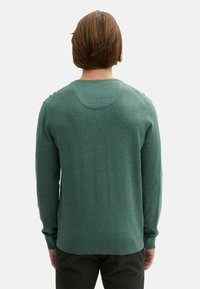 Pulover verde tricotat, cu mâneci lungi, guler rotund și manșete și tiv cu nervuri. Textură netedă, cu o formă ușor adaptată.