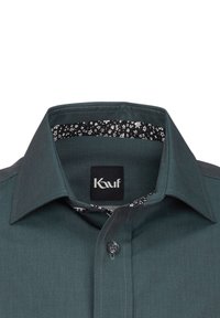 Camicia di colore turchese con colletto allargato, dotata di chiusura a bottone e di un rivestimento interno del colletto a motivo in bianco e nero. L'etichetta riporta la scritta "Kauf."