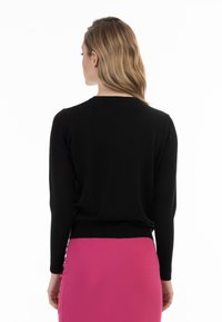 Schwarzer Strickpullover mit langen Ärmeln und Rundhalsausschnitt, kombiniert mit einem leuchtend rosa Bleistiftrock. Glatte Textur, enganliegendes Design.
