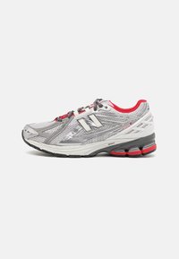 Szare i białe buty biegowe New Balance z czerwonymi akcentami, meshowym wierzchem, wyściełaną podeszwą i etykietą "1906R" po boku.