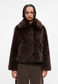 Casaco de pelo sintético castanho com um colarinho alto, mangas longas e uma textura suave, combinado com calças castanhas texturizadas.