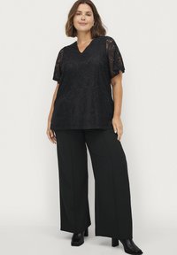 Zwarte kanten top met korte mouwen en V-hals, gecombineerd met wijde zwarte broek. Soepele textuur met bloemmotieven.