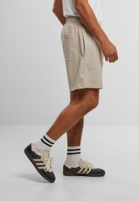 Beige Baumwollshorts mit einem elastischen Bund, seitlichen Taschen und entspannter Passform, kombiniert mit marineblauen und cremefarbenen Sneakers und gestreiften Socken.