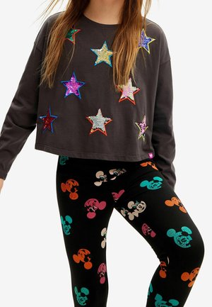 Sudadera gris recortada con estrellas de lentejuelas multicolores; combinada con leggings negros con patrones coloridos de Mickey Mouse.