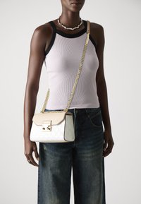 Bolso bandolera blanco y beige con patrón en relieve, correa de cadena dorada, forma rectangular y detalle de cierre metálico.