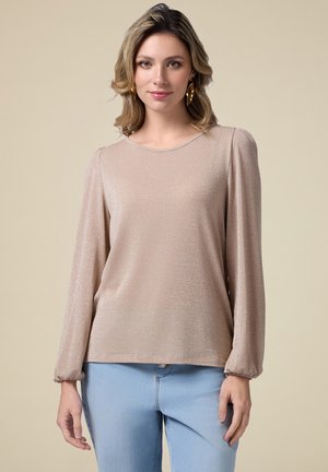 Top de manga larga en color beige, hecho de un tejido brillante; cuenta con un escote redondo y puños fruncidos, combinado con unos jeans de color azul claro.