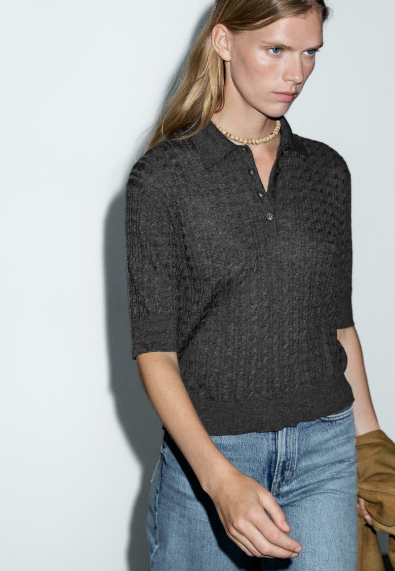 Grijs gebreid poloshirt met korte mouwen, voorzien van een gestructureerd patroon en een kraag, gecombineerd met lichtblauwe hoge taille jeans.