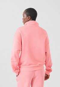 Roze fleece sweatshirt met hoge kraag, verlaagde schouders en geribde manchetten. Draagt met bijpassende broek, zachte textuur en ontspannen pasvorm.