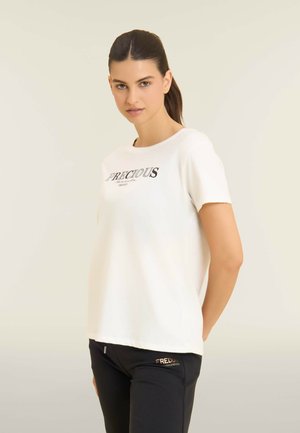 T-shirt bianco a maniche corte con la parola "PRECIOUS" in nero e dettagli in strass. Abbinato a pantaloni neri con il logo "FREDDY".