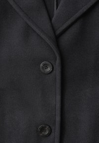 Black coat featuring a textured fabric with a smooth finish, single-breasted design, and round black buttons with a subtle embossed detail.