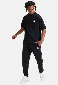 Svart bomullströja med rund hals och liten FILA-logotyp. I kombination med matchande svarta sweatpants med sidostrimma och logotyp. Vita sneakers.