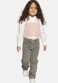 Top corto lavorato a maglia rosa con motivo a treccia, camicia bianca con bottoni, jeans grigi con strisce verticali argentate e sneakers bianche.
