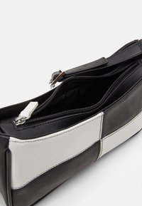 Black and white rectangular shoulder bag with a top zipper partially open, showing an empty black interior compartment.