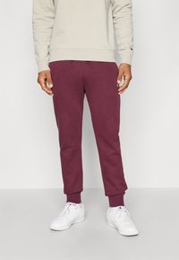 Pantalons de jogging bordeaux avec des poignets côtel�és, fabriqués à partir d'un matériau doux. Associés à un sweat-shirt gris clair et des baskets blanches.