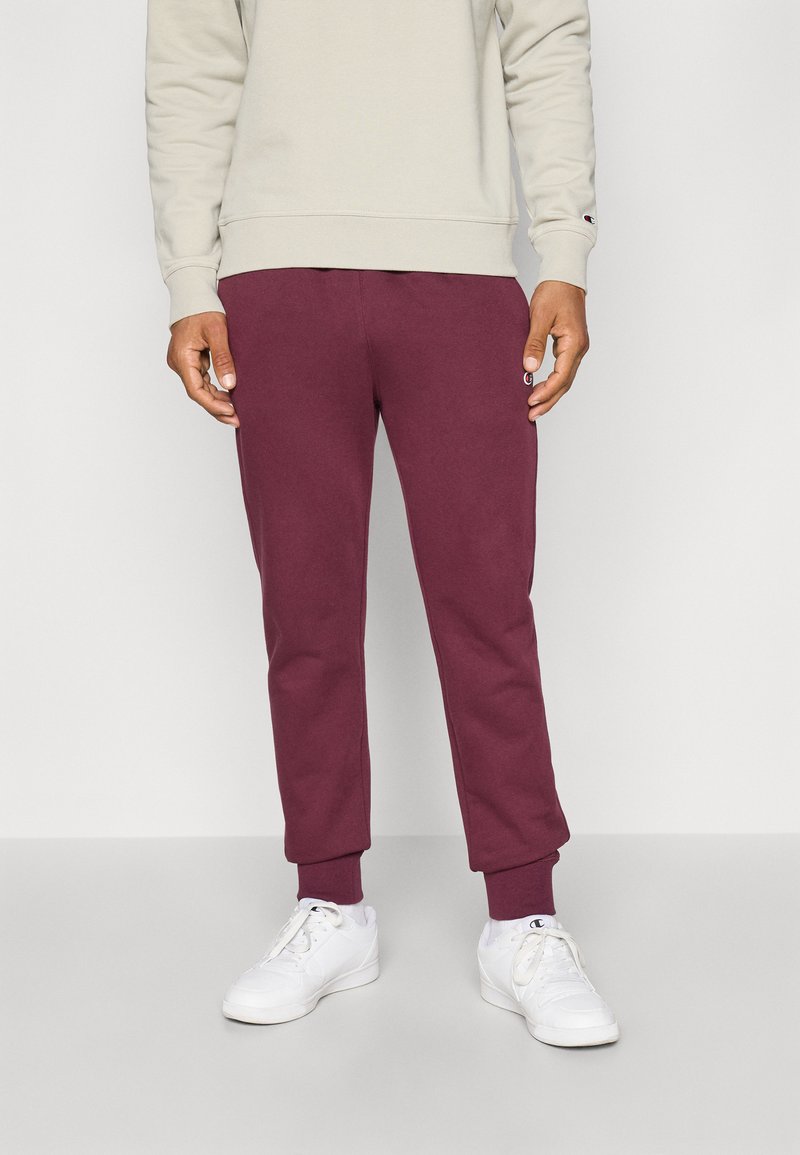 Pantalons de jogging bordeaux avec des poignets côtelés, fabriqués à partir d'un matériau doux. Associés à un sweat-shirt gris clair et des baskets blanches.