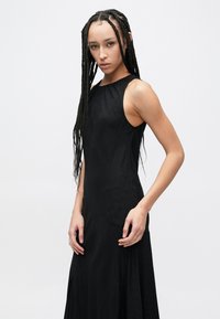 Vestido preto sem mangas com gola alta, textura suave e padrão subtil. Ajustado na parte superior, alargando-se em direção à bainha.