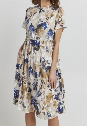 Sukienka w kwiaty z abstrakcyjnymi niebieskimi, brązowymi i różowymi wzorami na jasnobeżowym tle. Krótkie rękawy, zapięcie na guziki oraz boczne kieszenie.
