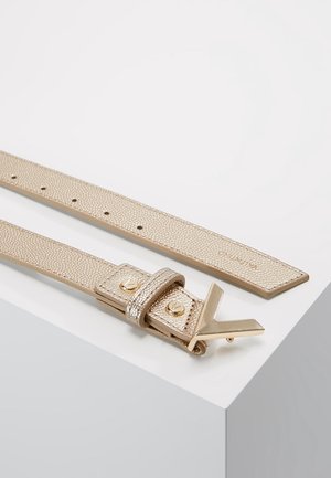 Gold texturierter Ledergürtel mit goldener V-förmiger Schnalle und zwei goldenen Nieten, flach auf einer weißen Oberfläche liegend.