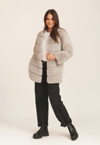 Gray faux fur jacket with a boxy shape and horizontal stripes. Long sleeves and a soft texture. Paired with black wide-leg jeans and platform boots.