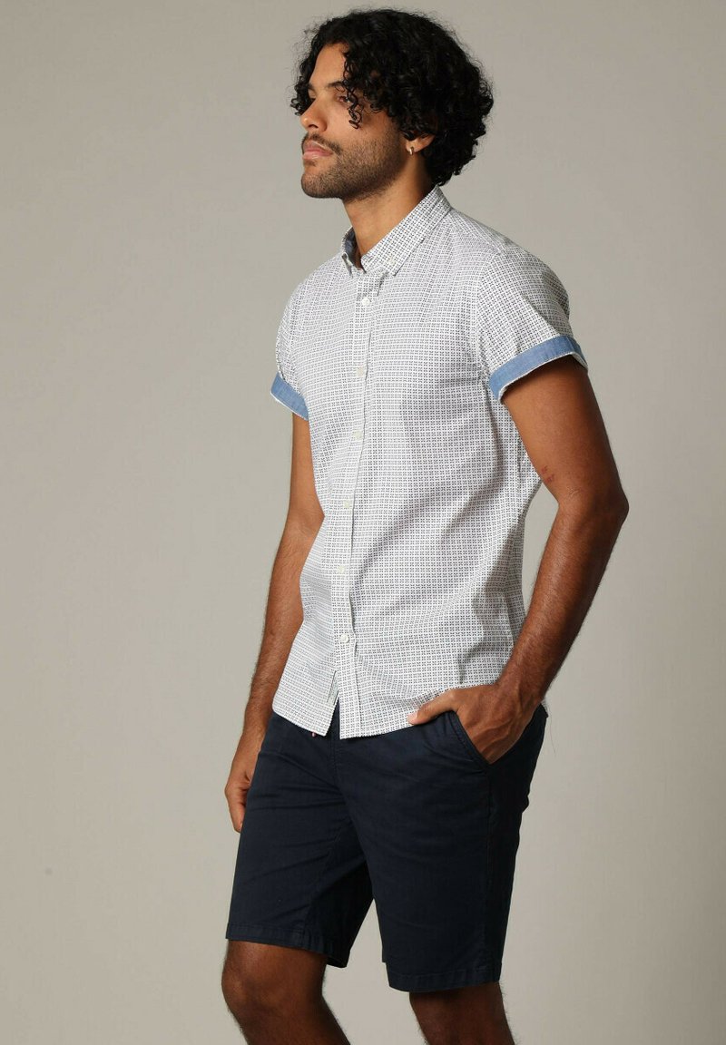 Korte mouwen, knoopsluiting shirt met een patroon van witte stof en blauwe manchetten, gecombineerd met donkerblauwe shorts. Zachte textuur.