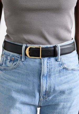 Zwarte leren riem met een gouden gesp, gedragen over lichtblauwe denim jeans, vergezeld van een grijze geribde tanktop.