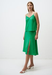 Camisole en soie verte avec des fines bretelles et une jupe assortie avec une fente à l'avant. L'ensemble présente une texture lisse et une coupe décontractée.