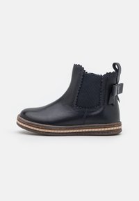 Botte cheville en cuir navy avec panneau élastique sur les côtés, bords festonnés et détail en nœud à l'arrière. Dotée d'une semelle texturée et d'une semelle intermédiaire cousue.