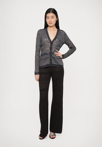 Fekete és szürke, hosszú ujjú, nyitott kötésű kardigán V-nyakkal és gombos rögzítéssel, fekete, trapéz szabású, texturált nadrággal párosítva.