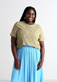 Olive green textured blouse with short sleeves, paired with a light blue, flowing maxi skirt. Round neckline with decorative pattern details.