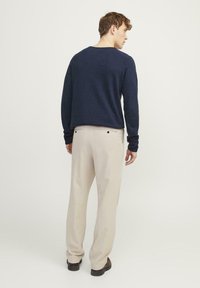 Granatowy sweter wykonany na drutach o luźnym kroju, w połączeniu z beżowymi spodniami. Materiał ma miękką fakturę, a spodnie mają tylne kieszenie.