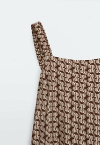 Brun kjole med mønstret design i creme, med en rynket skulderrem. Letvægtsstof, glat tekstur og subtil glans.