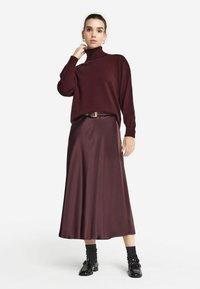 Burgundowy sweter z golfem, luźny krój; satynowa burgundowa spódnica maxi; czarne buty z błyszczącym wykończeniem; teksturowane czarne skarpetki.