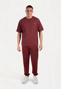 Vinröd t-shirt med korta ärmar och en liten logga, kombinerad med matchande vinröda joggers. Bärs med vita sneakers. Mjuk textur.