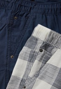 Deux paires de boxers pour hommes pliés, un uni bleu foncé et un blanc à motif carreaux bleu, tous deux avec braguette à boutons.