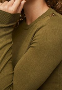 Pull en tricot vert olive à manches longues, avec des poignets côtelés et des boutons latéraux. Texture lisse avec une silhouette ajustée.