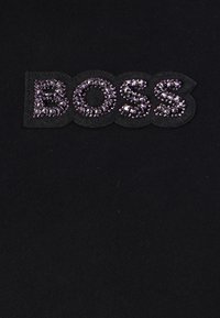 Svart tyg med ordet "BOSS" i en djärv, texturerad lapp prydd med lila paljetter. Slät yta med subtil glans.
