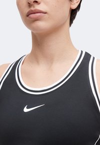 Gros plan d'une personne portant un haut de sport noir sans manches avec un bord rayé blanc et un logo Nike blanc sur le devant.