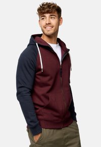Sudadera con cremallera en color burdeos y marino, con cordones, puños acanalados y dos bolsillos frontales. Tejido suave con mangas de color contrastante.