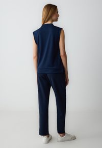 Top senza maniche blu navy con una vestibilità rilassata, abbinato a pantaloni coordinati. Tessuto morbido, design informale, e completato da sneakers bianche.