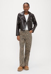 Brūna mākslīgās ādas īsā motociklu jaka virs baltas T-krekla, kopā ar bēšām un melnām zebras raksta platajiem biksēm un platformas zābakiem.