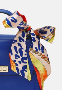 Blå läderhandväska med en dekorativ mönstrad scarf knuten vid handtaget. Scarfen har djurmönster och livliga färger som orange och gult.
