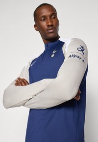Navy long-sleeve training top with a half-zip collar, light gray sleeves, Tottenham logo, and Alipay branding on the right sleeve.